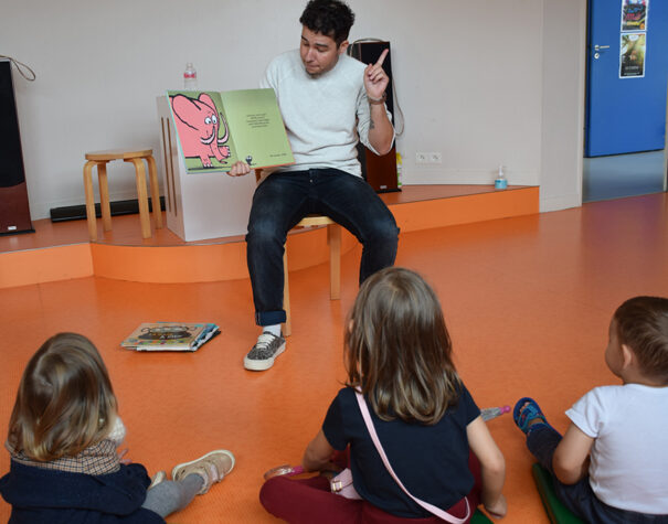 Un homme qui lit une histoire en montrant les images du livre à des enfants assis au sol