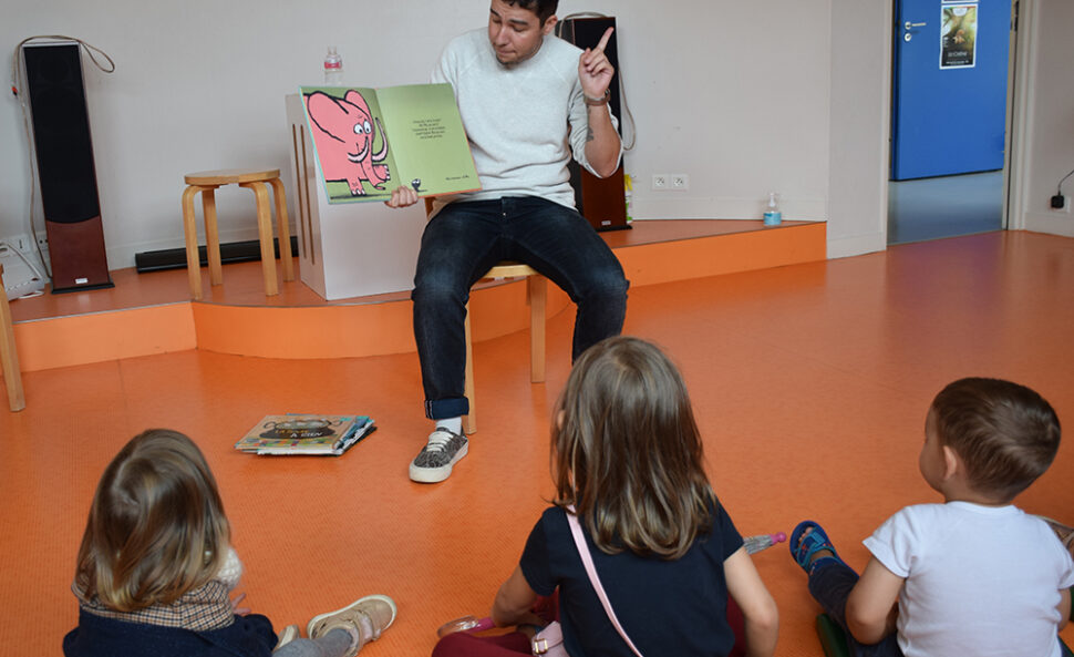 Un homme qui lit une histoire en montrant les images du livre à des enfants assis au sol