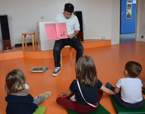 Un homme qui lit une histoire en montrant les pages du livre à des enfants assis.