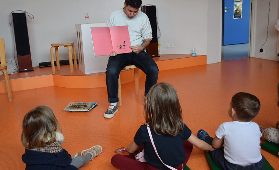 Un homme qui lit une histoire en montrant les pages du livre à des enfants assis.